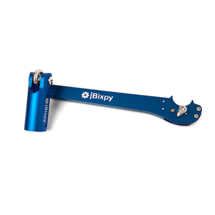 Bixpy Pole Steering adapter side view. A cylinder with an arm branching out from it and a groove for a pole to be set in. The adapter is royal blue with the Bixpy logo in white.