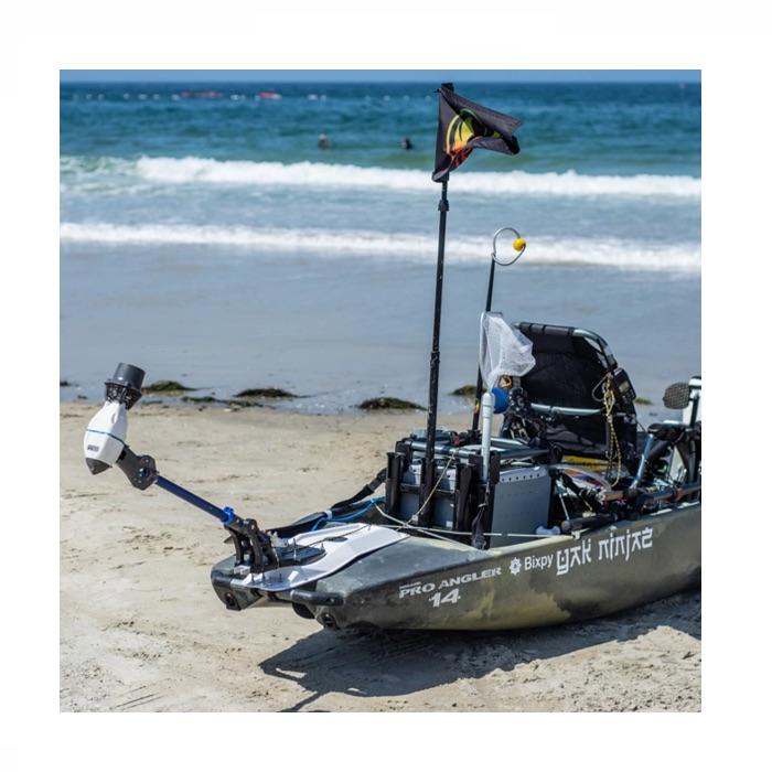 Bixpy Universal Power Pole Kayak Adapter  is shown in place on a kayak on the beach.  The motor is fully hinged and out of the water.
