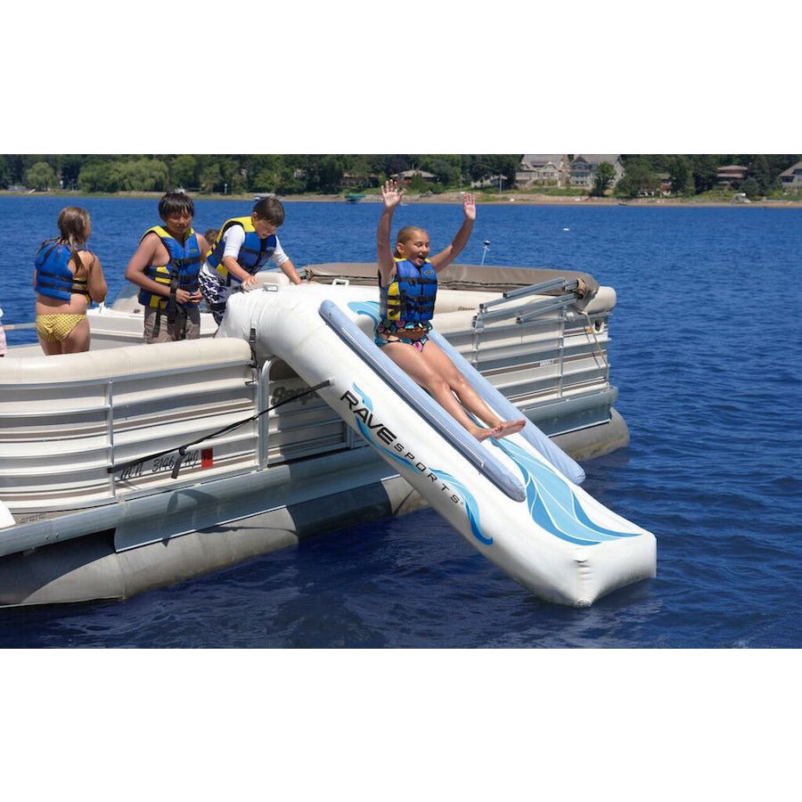 Side view of a girl sliding down a Rave Inflatable Pontoon Slide with 3 kids standing on the pontoon.  Sliding into the lake.