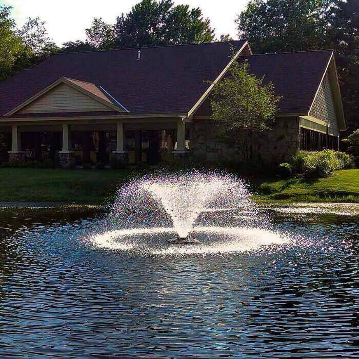Scott Aerator DA-20 Display Aerator 1/3 Hp Floating Pond Fountain spraying its trumpet shaped water fountain spray in a neighborhood lake with a house in the background.  Very pleasing floating aerator fountain. Also known as a Small Pond Aerator Fountain.