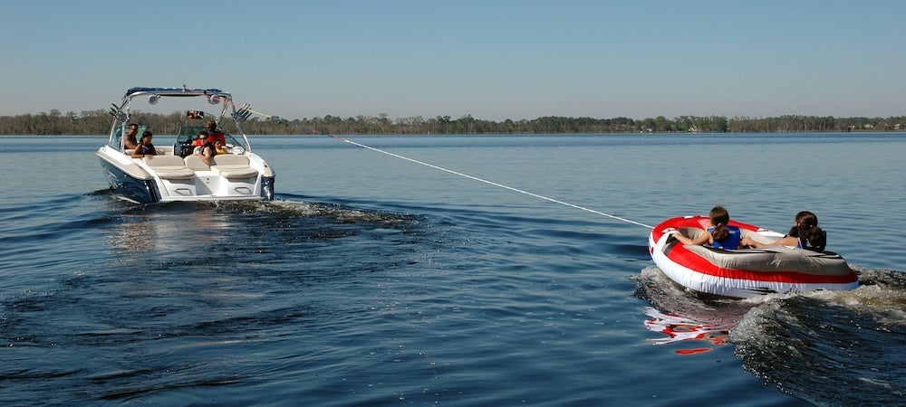 How Boating Tubes Will Enhance Your Summer Fun Blog. A red and white boating tube is being pull behind a speedboat on the lake.