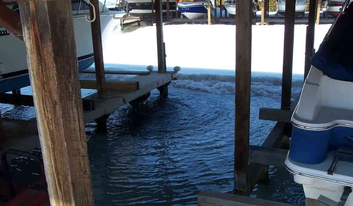 An Ice Eater is in use protecting a marina from ice damage.  There is ice and snow in between the two multi-boat docks but in the slips where the ice eater is there is no ice.