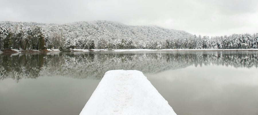 Black and white image of a small lake with a long dock covered in snow. 