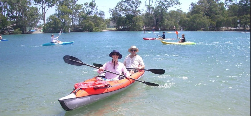 A couple enjoys their inflatable kayak for sale on a lake.  There are several others using inflatable kayaks on the water.