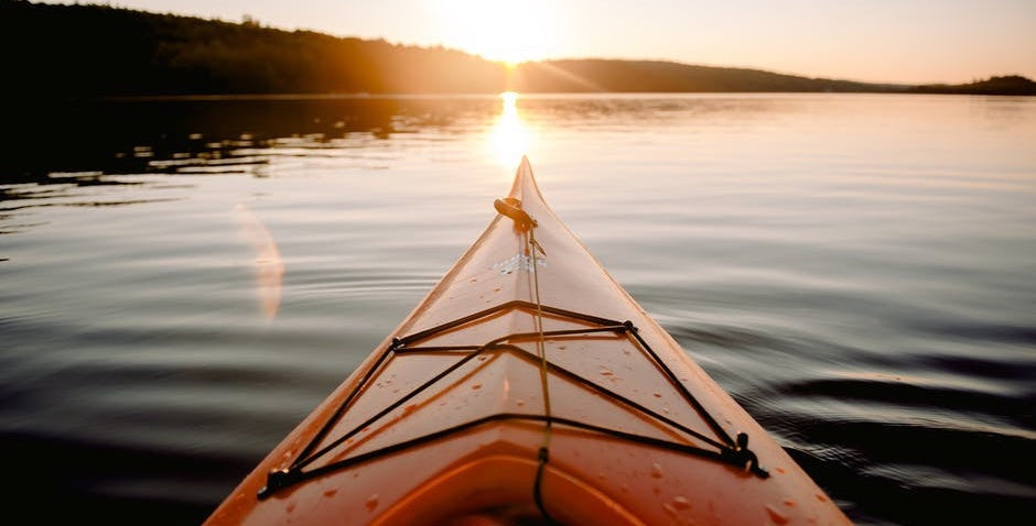 We get the point of view angle as if we are on an orange kayak easing across the calm waters of a lake toward a setting sun over the thick trees.