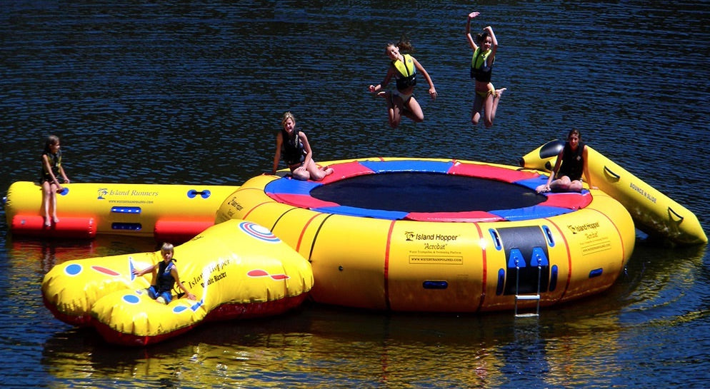 Water Trampoline Floating Water Park showing 6 kids playing on a water trampoline on the lake.  The water trampoline is yellow and features blue and red highlights.