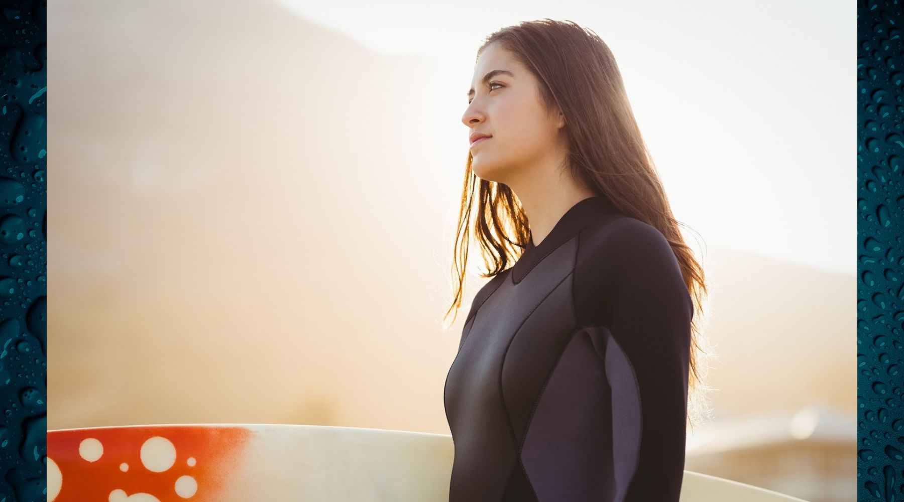 Woman in a wetsuit holding a surfboard.
