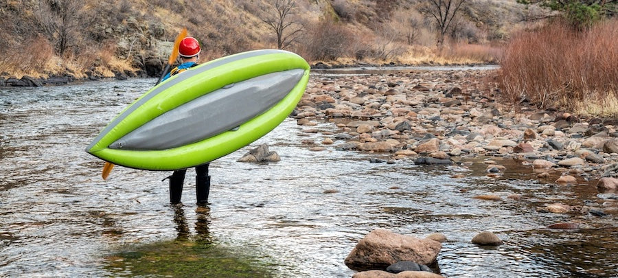 A man walks through a shallow creek with his light green inflatable kayak. Winter care tips for Inflatable Kayaks and Paddleboards