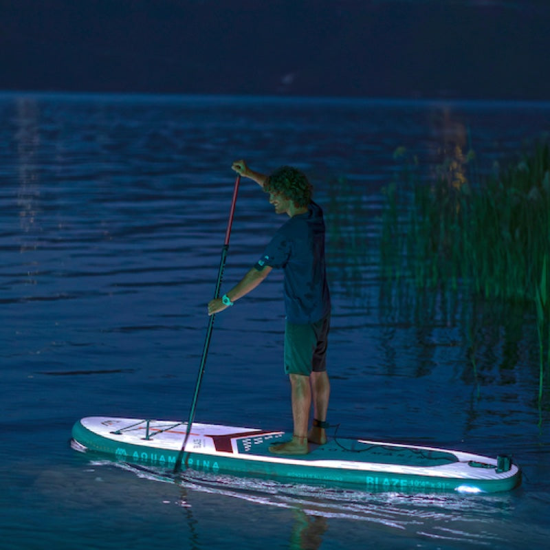Person paddleboarding on a lake at night with illuminated board