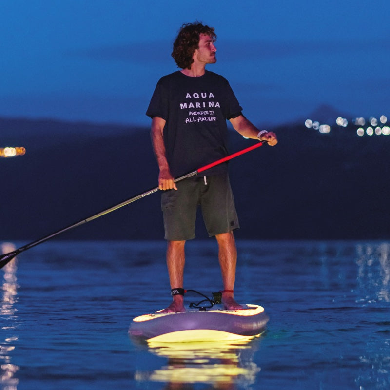 Man paddleboarding at night on a body of water with illuminated sup.