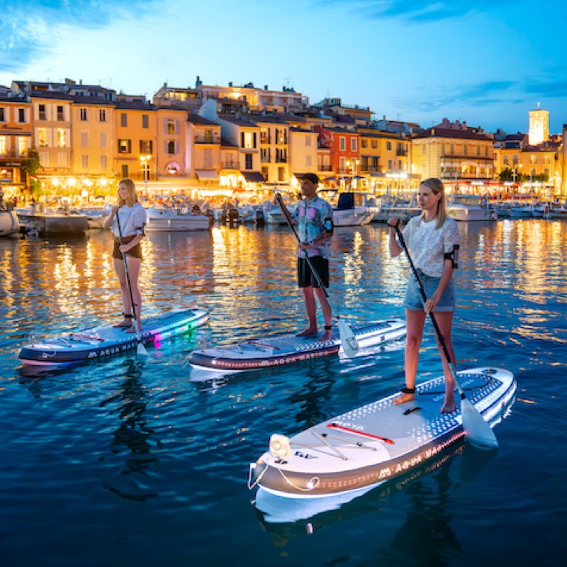Three people paddleboarding on a body of water with a cityscape in the background.