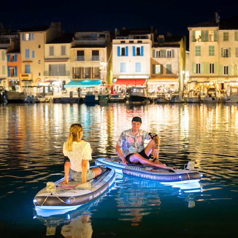 Two people on paddleboards at night in a waterfront cityscape.