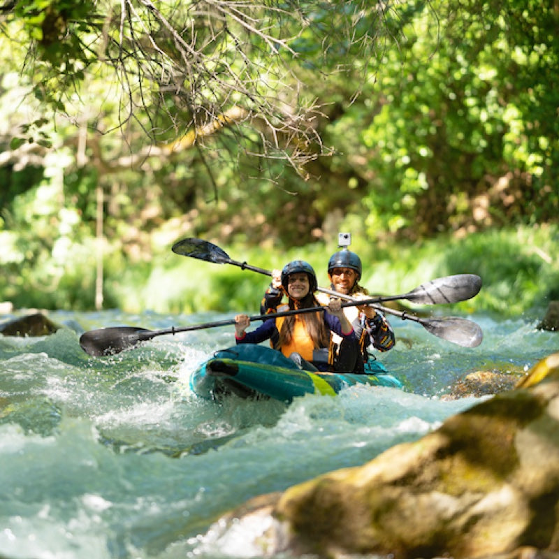 Two people kayaking in a river with trees and rocks in the background