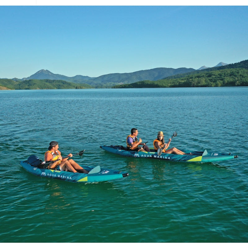 Three people in inflatable kayaks on a calm lake with mountains in the background