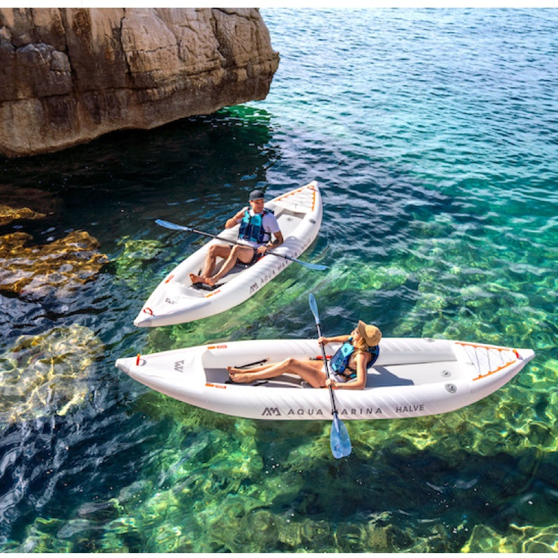 Two people in inflatable kayaks near a rocky cliff with clear blue water.