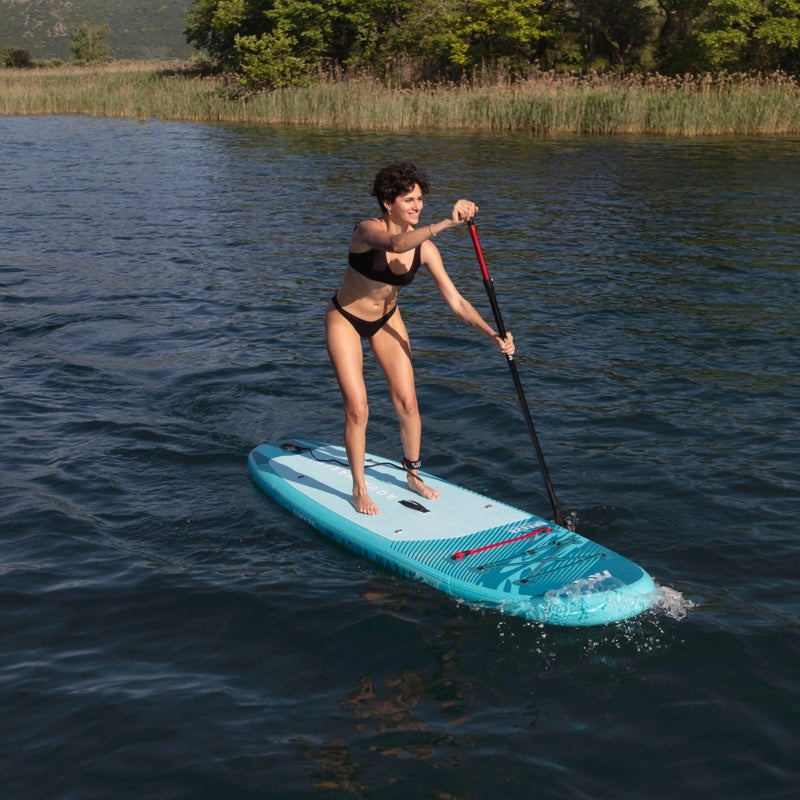 Woman paddleboarding on a lake with reeds and trees in the background