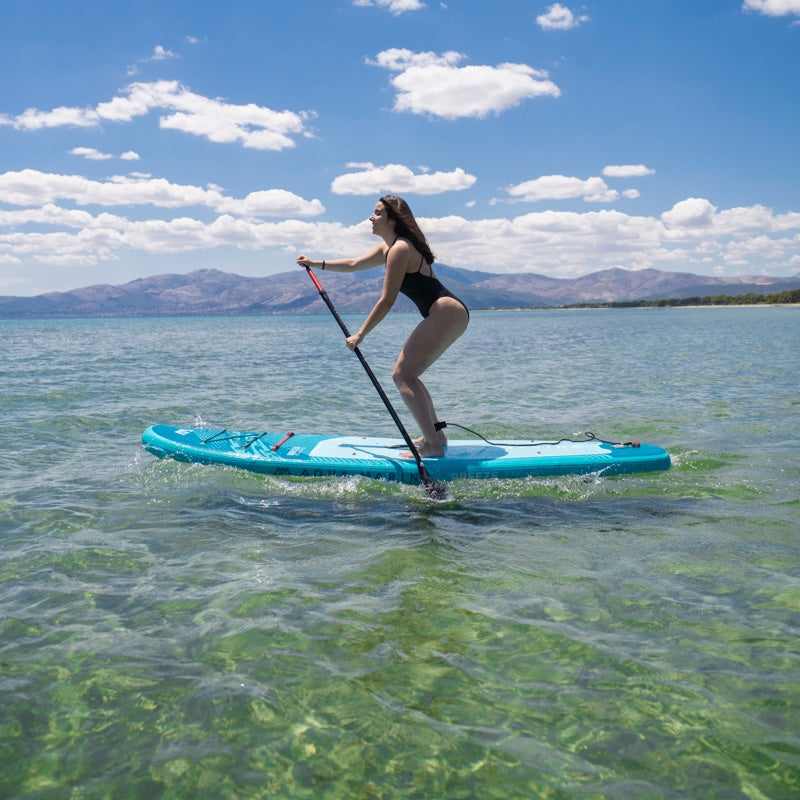 Person paddleboarding on a clear body of water with mountains in the background