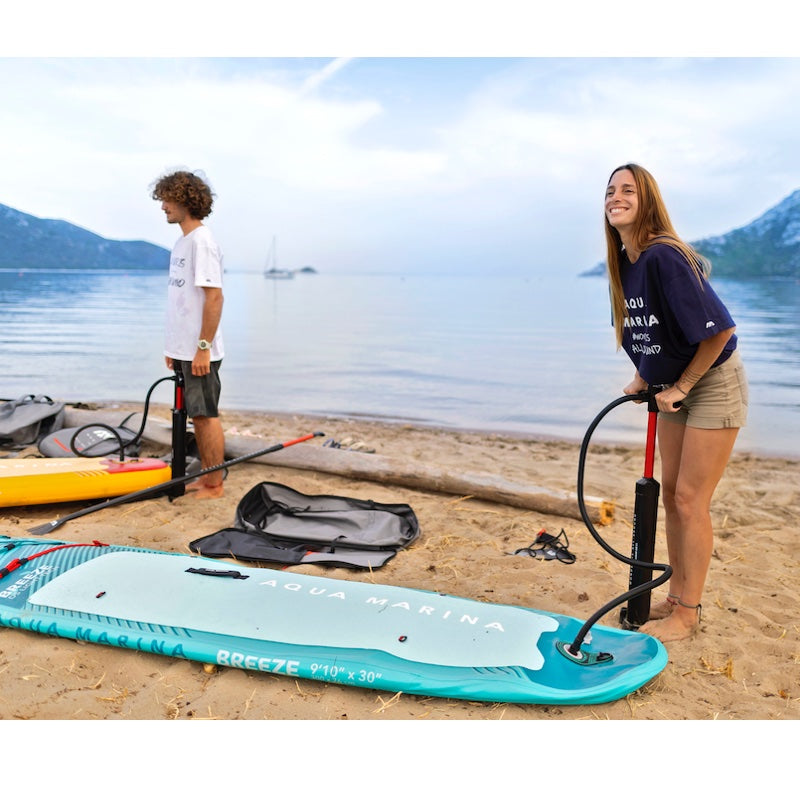 Two people with a paddleboard on a beach near water; inflating