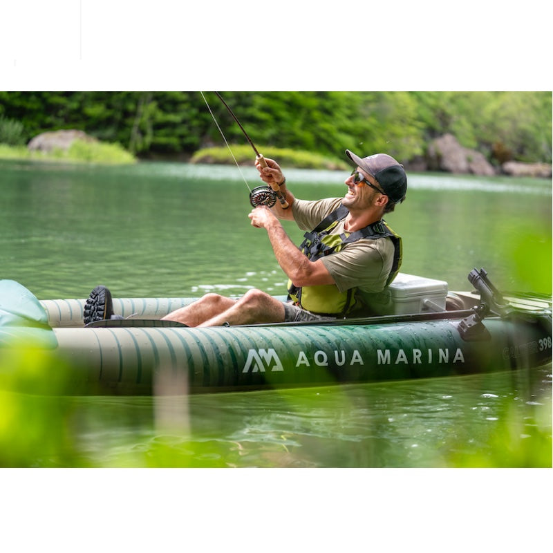 Man fishing in an Aqua Marina angler 
kayak on a calm lake with trees in the background