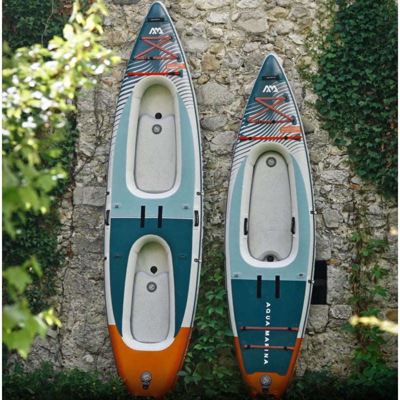 Two hybrid kayak-paddle boards leaning against a stone wall with greenery.