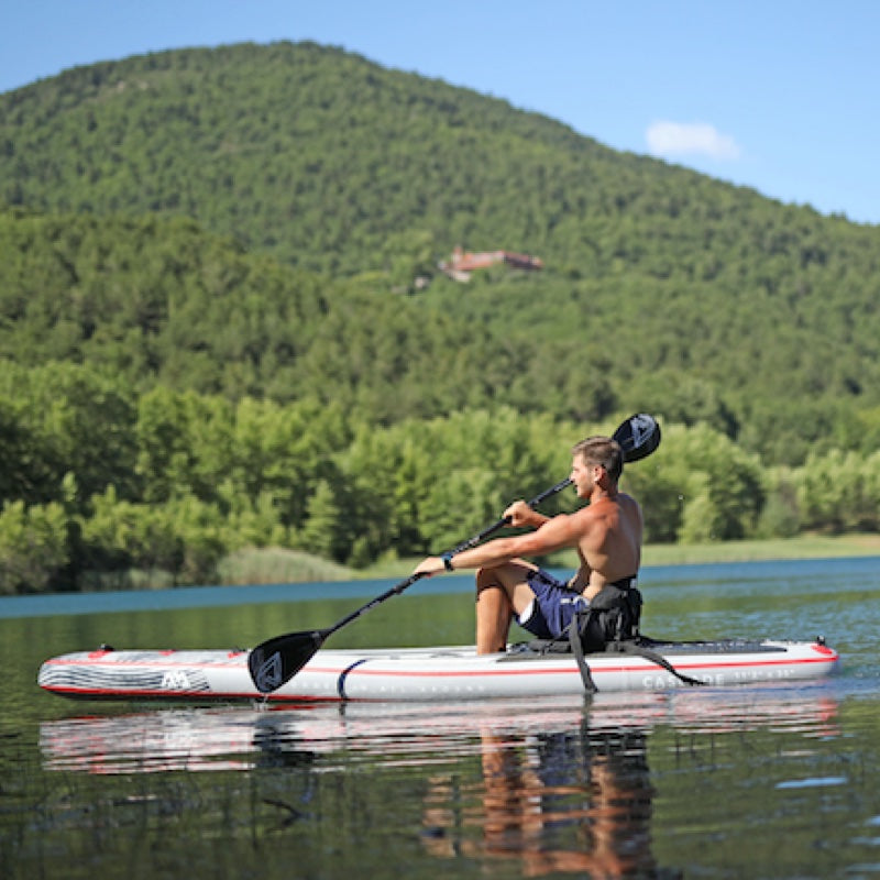 Man sit down paddleboarding on a lake with a mountainous background