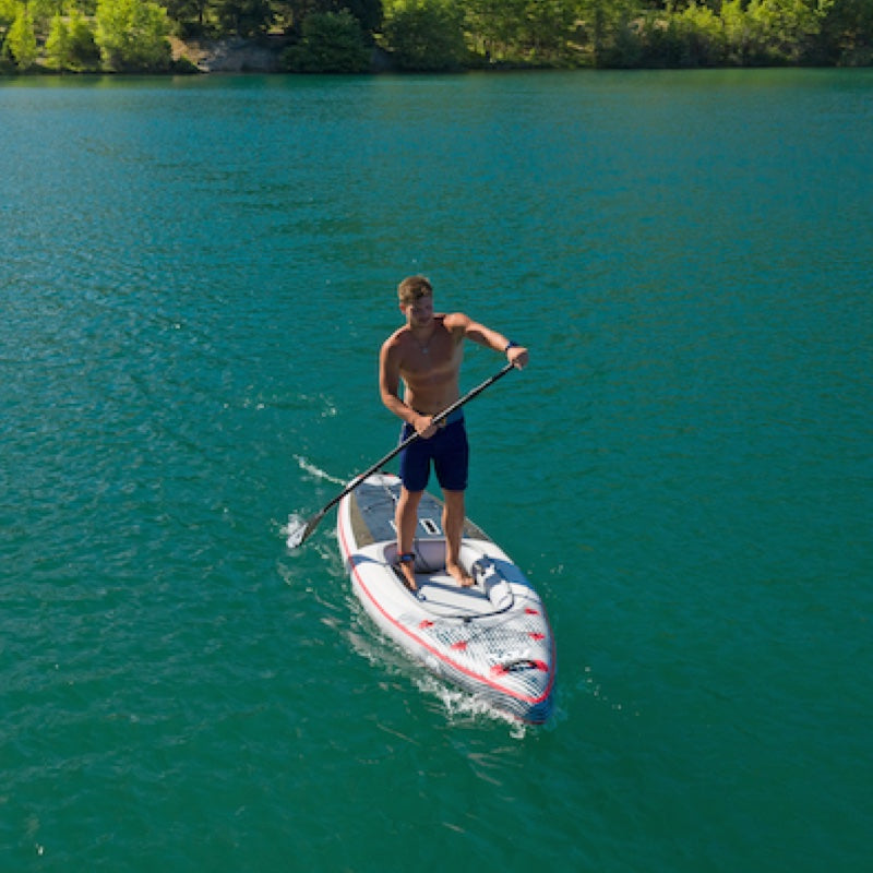 Man paddleboarding on a clear blue lake with trees in the background