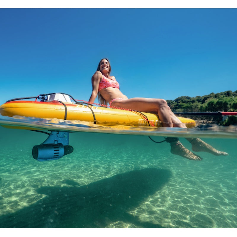 Woman lying on a yellow inflatable SUP in clear blue water with a boat in the background.