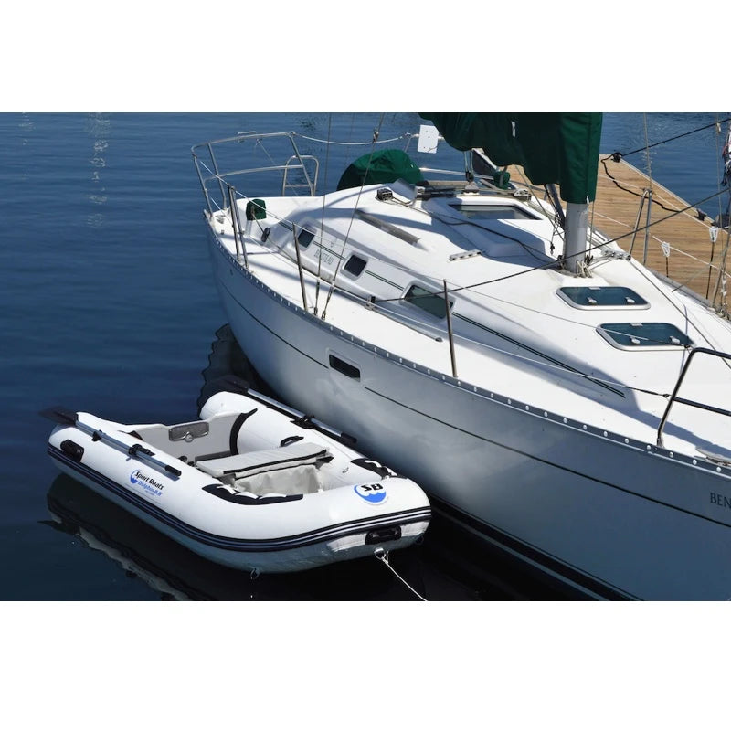 Small inflatable boat attached to a larger sailboat on calm water.