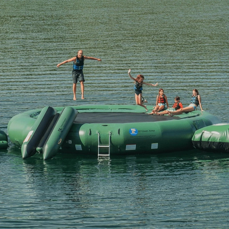Children playing on a large green inflatable trampoline floating on water.
