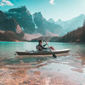 A man paddles his kayak down a crystal clear river in the mountains.