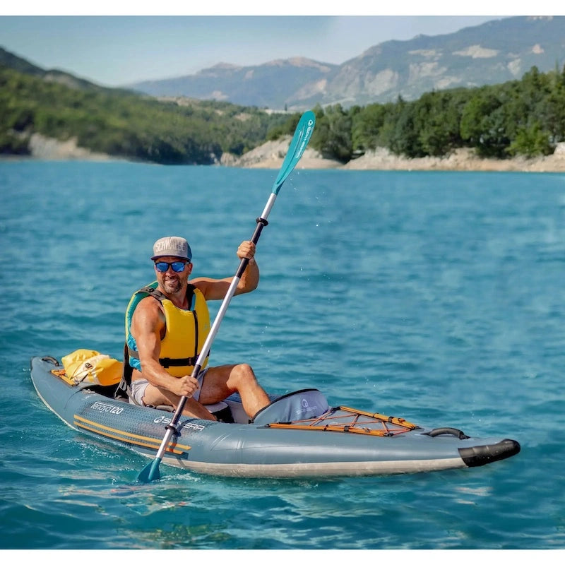Man paddling a Tenaya kayak on a calm lake with mountains in the background