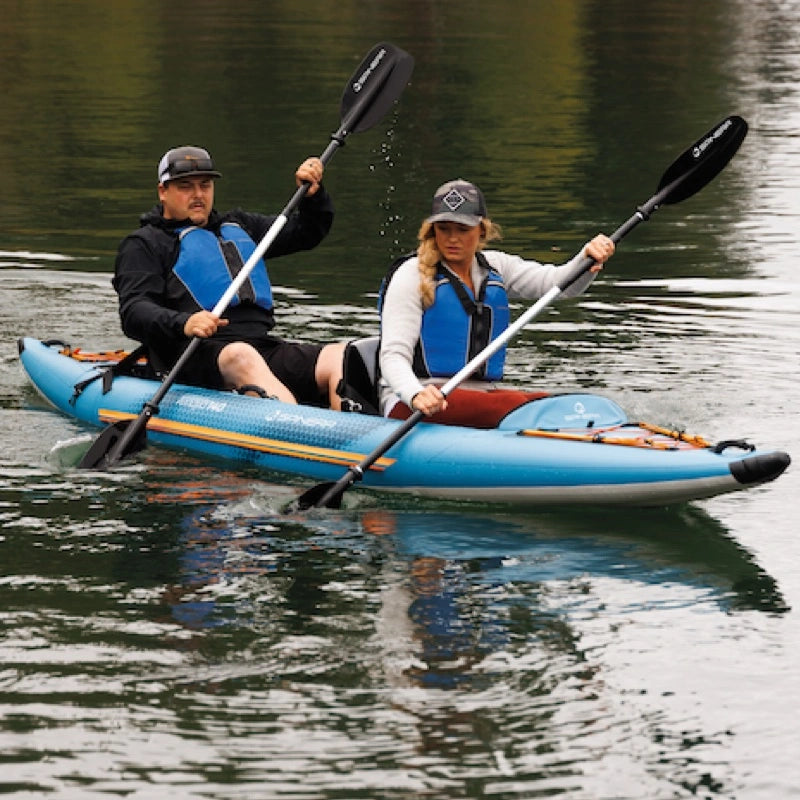 Two people paddling a blue inflatable kayak on calm water.