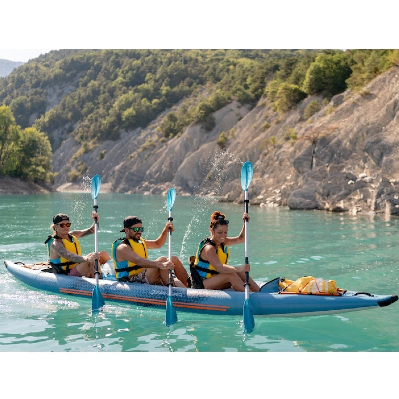 Three people kayaking on a calm lake with a scenic background