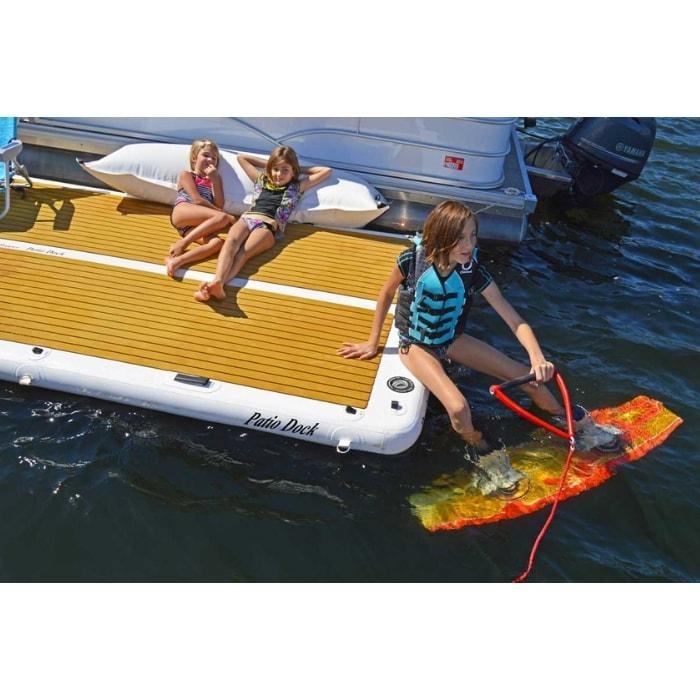 Island Hopper Patio Dock Floating Swim Platform makes a great launch point for wakeboarding. Here you see a couple of girls laying down on the inflatable floating dock while a young boy sits on the edge with his feet braced into a wakeboard waiting to take off.