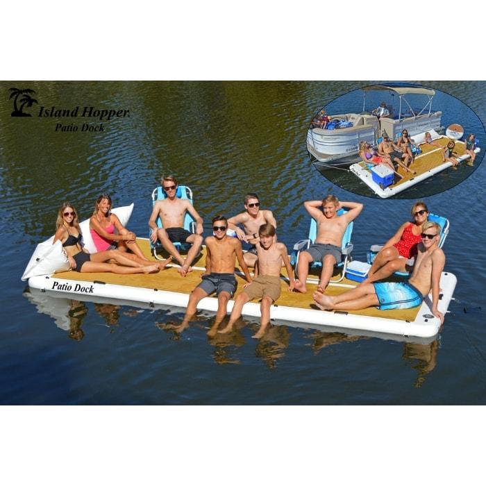 Island Hopper Patio Dock Floating Swim Platform Inflatable Dock is shown in the middle of a lake with 10 people on board. The inflatable dock is remaining perfectly buoyant and some of the people are sitting while others are in chairs. In the background there is another Island Hopper Inflatable Dock up against a pontoon.