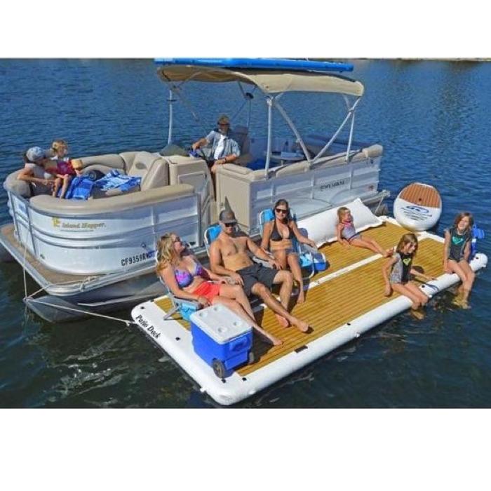 Island Hopper Inflatable Dock for Sale Floating Swim Platform is shown attached to a pontoon with 6 people relaxing and enjoying a day on the water. There are people sitting directly on the EVA foam surface and there are also people in chairs sitting on the inflatable floating dock as well as a cooler.
