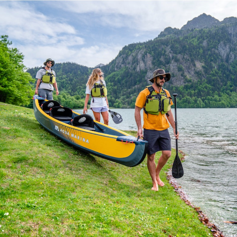 Two people carry a canoe and paddles near a lake with mountains in the background