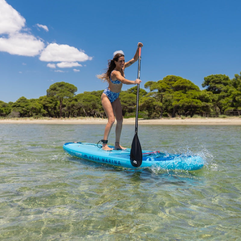 Woman paddleboarding on a clear body of water with trees and beach in the background