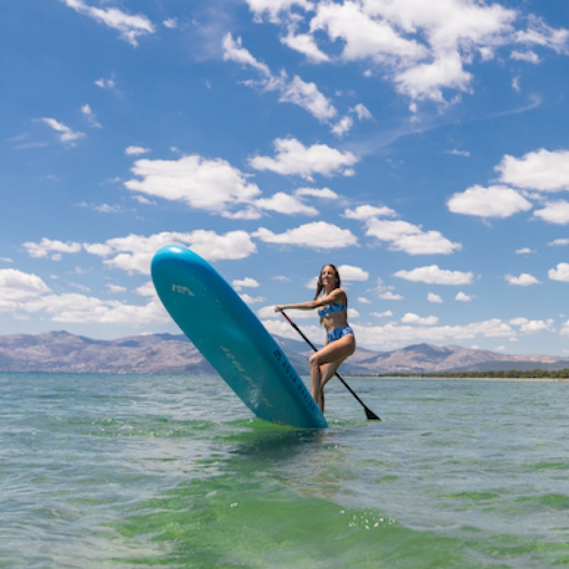 Woman paddleboarding on a lake with mountains and blue sky in the background