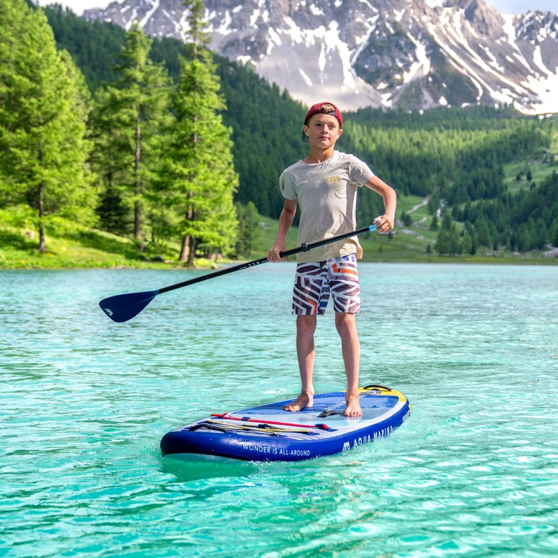 Boy on a stand-up paddleboard in a mountainous lake