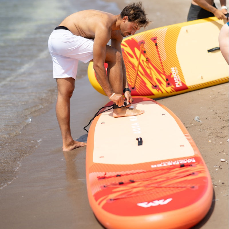 Man preparing a paddle board on the beach with another surfboard in the background.