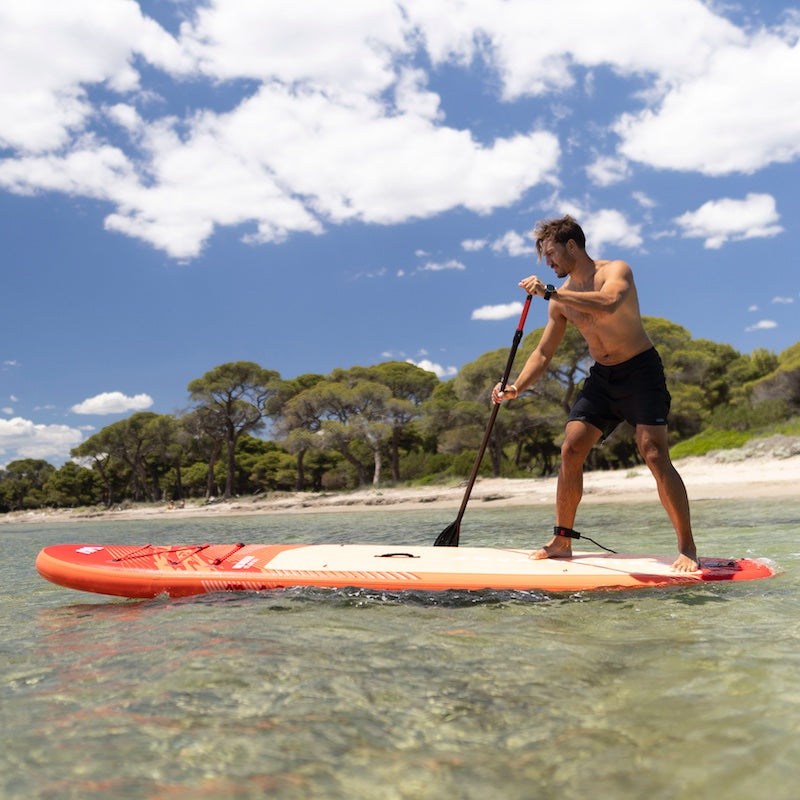 Man paddleboarding on a clear day with trees and blue sky in the background