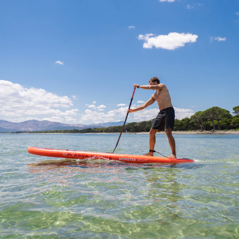 Man paddleboarding on a clear body of water with a blue sky and green trees in the background.