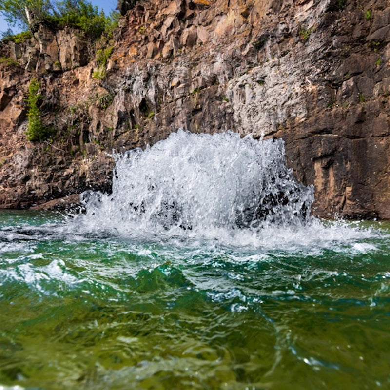 Water cascading up out of the water near a rocky cliff