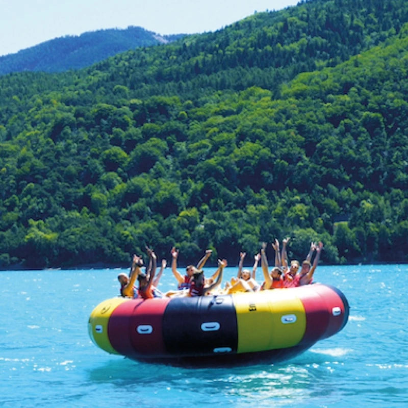 Group of people on a Endless Ride 8–12 spinning tube in a lake with green mountains in the background