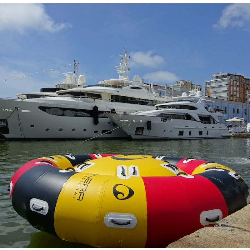 Inflatable boat tube with colorful design in front of large yachts on a dock.