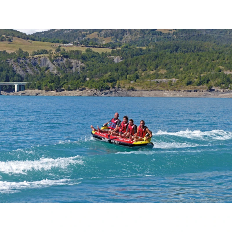 Four people on a red and yellow inflatable tube in a lake with mountains in the background