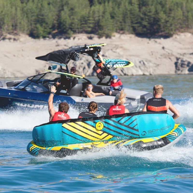 People on a blue and yellow towabletube being pulled by a boat on water with trees in the background.