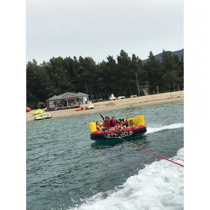 Inflatable boat tube with people on a lake, surrounded by trees and buildings.