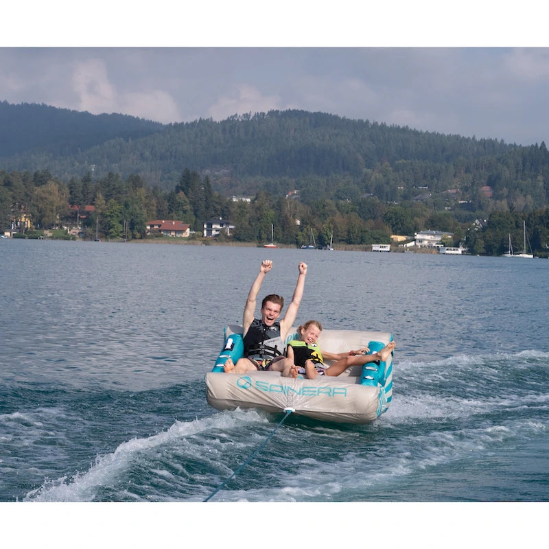 Two people on a inflatable tube in a lake with mountains in the background